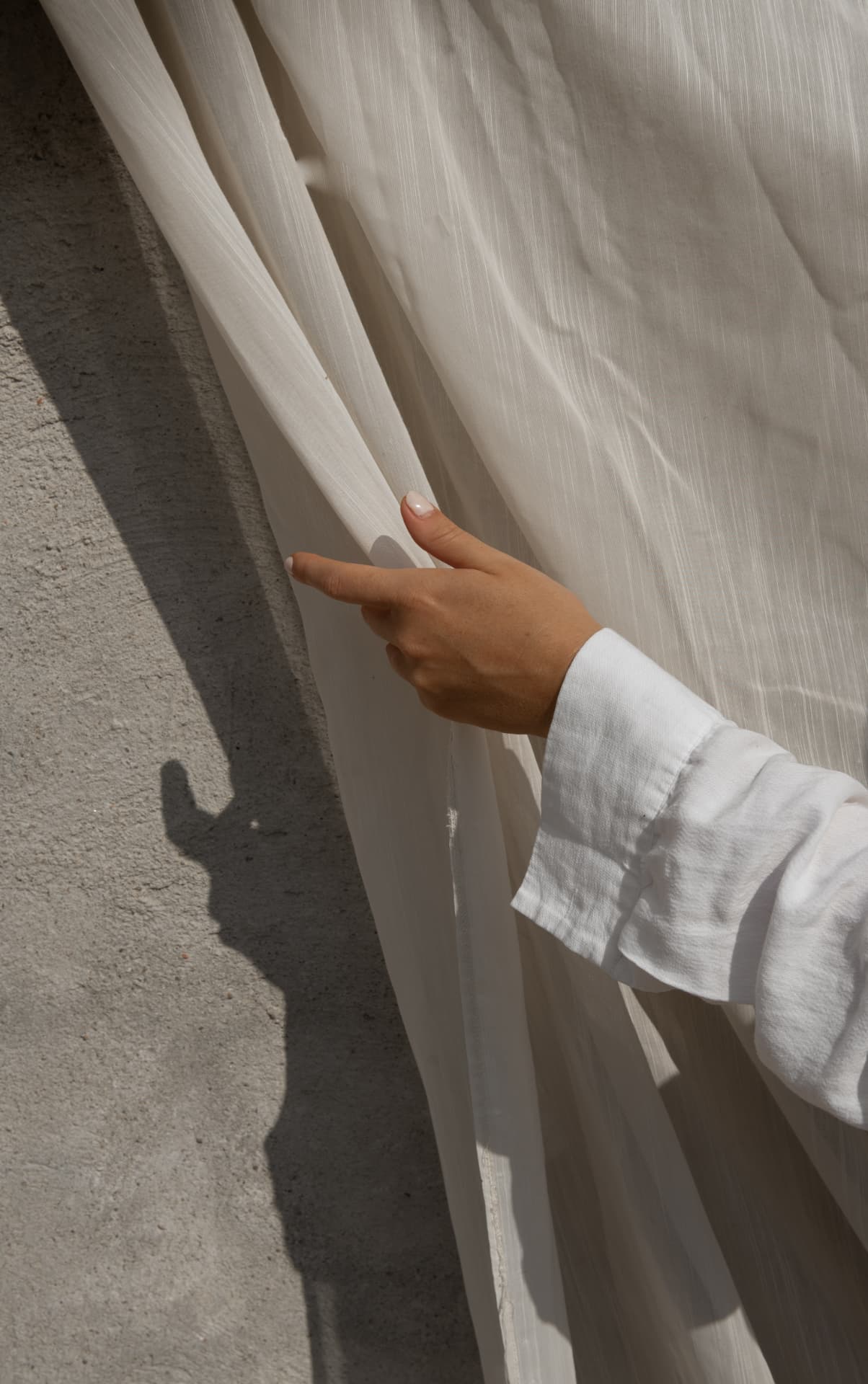 A hand drawing back a sunlit linen curtain